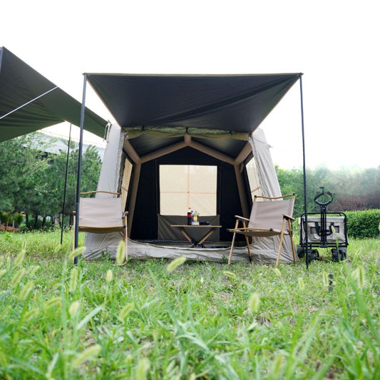 Beige 3-4 person inflatable ridge tent with hexagonal blackout canopy, outdoor furniture, and screen porch in grassy glamping setup with chairs and table