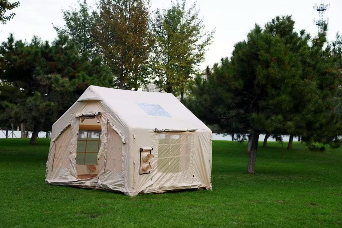 A large beige inflatable tent pitched on a grassy field, surrounded by trees under a cloudy sky.