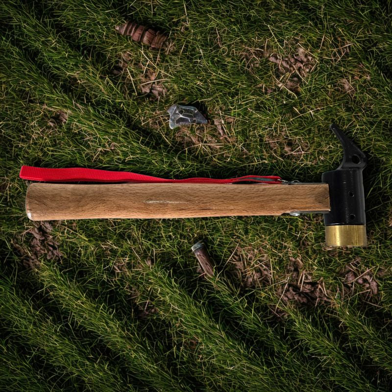 Camping mallet hammer with wooden handle, black metal head, brass peg puller, red lanyard, on green grass with scattered tent pegs