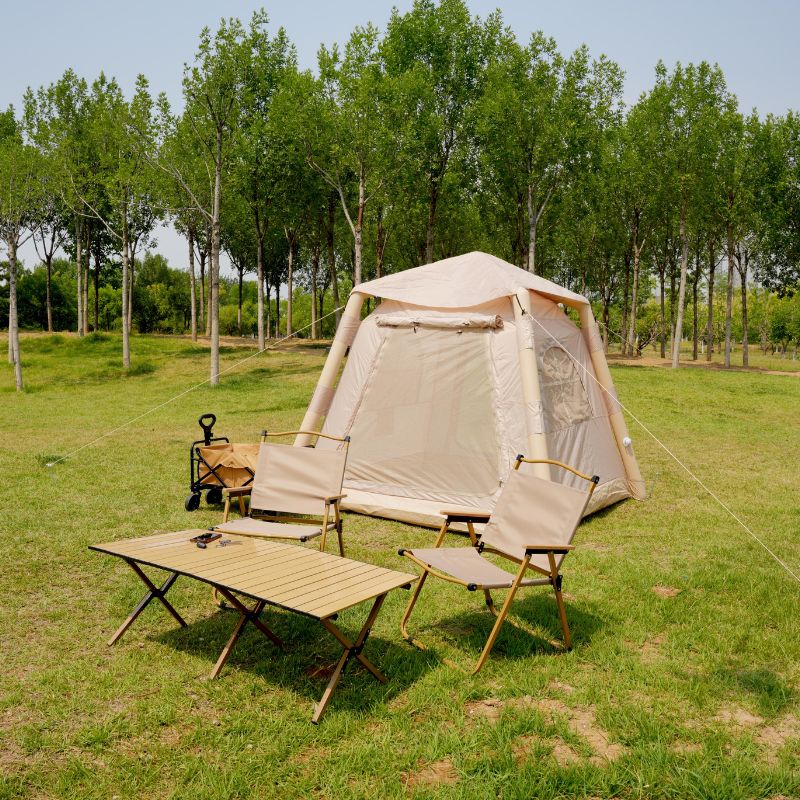 Camping setup with a tent, chairs, and table in a grassy area with trees.