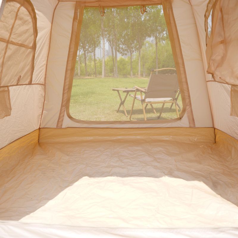 Inside of a beige tent with a view of greenery and a table outside.