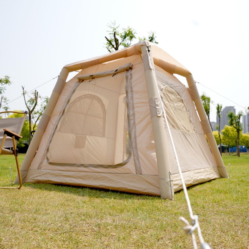 Beige camping tent with a chair on grassy area with trees and buildings in the background