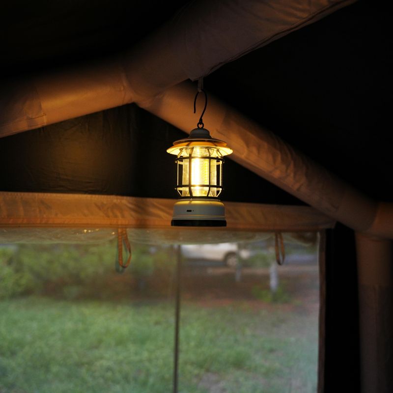 Lighted lantern hanging inside a tent with a view of a grassy area outside.