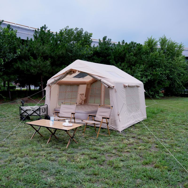 Beige camping tent with furniture on a grassy area with trees in the background