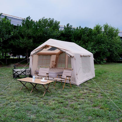 Beige camping tent with furniture on a grassy area with trees in the background