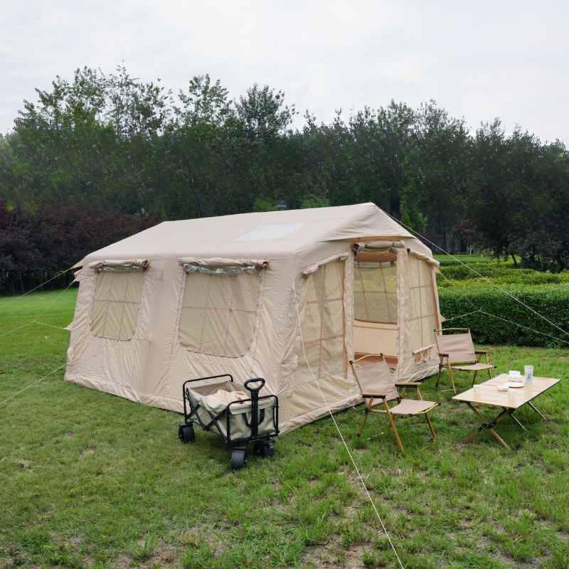 Beige camping tent with furniture and supplies on a grassy area with trees in the background