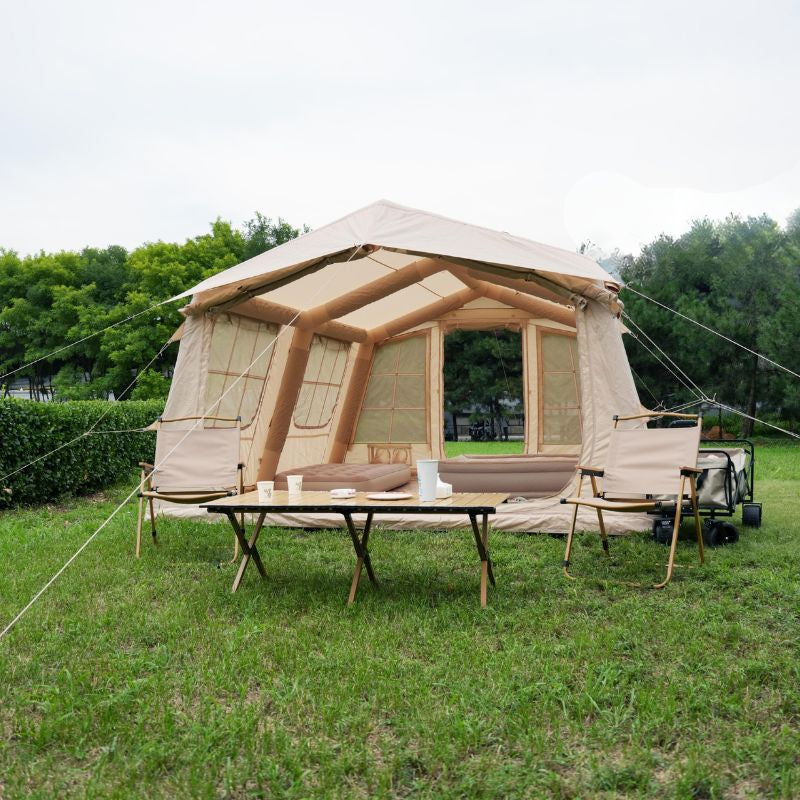 Large beige tent with wooden frame on grassy area with trees in the background