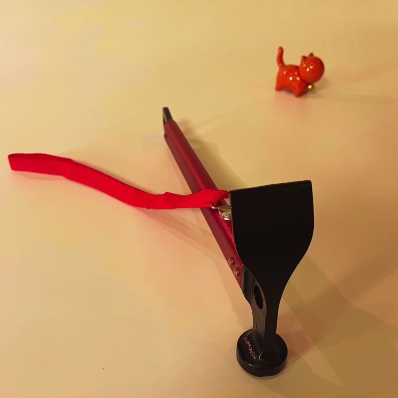 Red slingshot with a black grip on a beige background