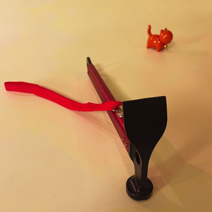 Red slingshot with a black grip on a beige background