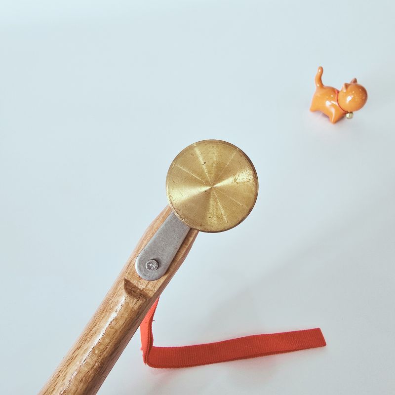 Small orange cat figurine next to a gold wheel and wooden tool on a light blue background