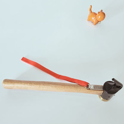 Small tool with wooden handle, red cord, and black head on a light gray background