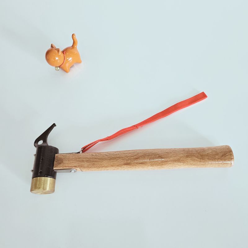 Small hammer with wooden handle and brass head on a light blue background