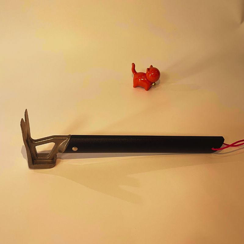 Long tool with a black handle and metal head on a beige background, with a small red object nearby.