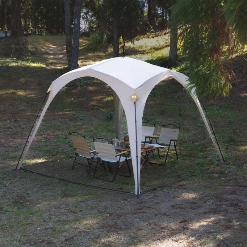 Outdoor canopy tent set up in a grassy area with chairs and a table underneath.
