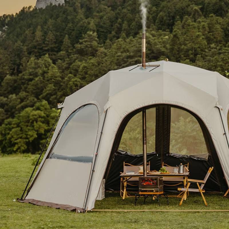 Large dome-shaped tent with a table and chairs set up outdoors in a forested area.