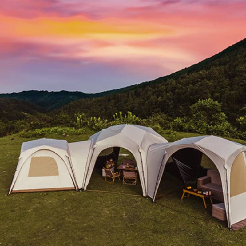 Two connected camping tents with a sunset over a mountainous landscape.