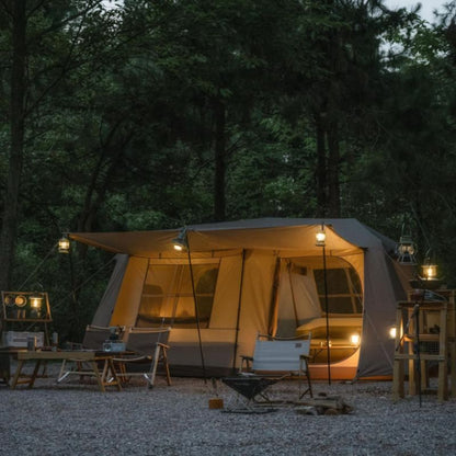 Camping tent with outdoor furniture in a forest setting at night.