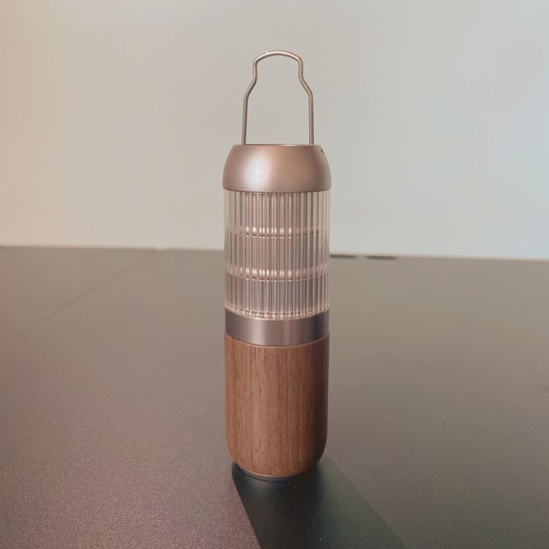 Tall cylindrical container with wooden base and metallic top on a reflective surface