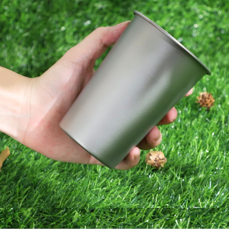 Hand holding a metallic cup against a grassy background