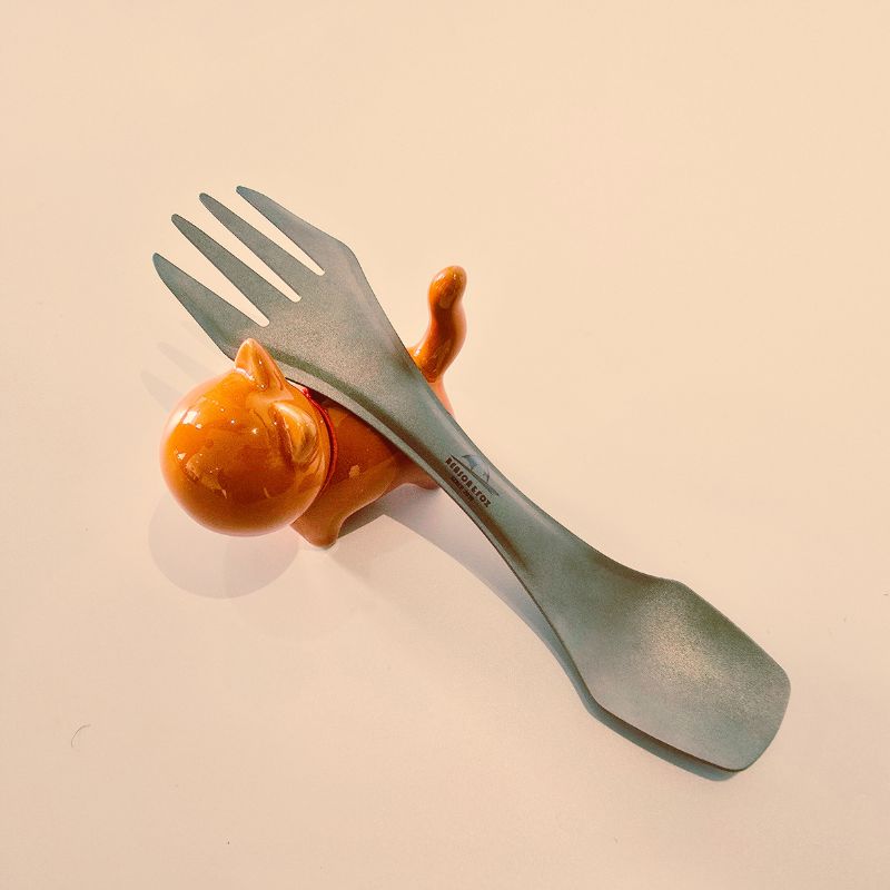 Green fork with a small orange cat-shaped object on a beige background
