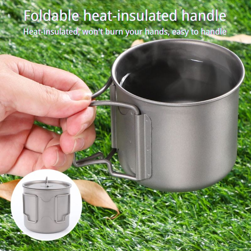 Metal mug with a foldable heat-insulated handle held by a hand on grass
