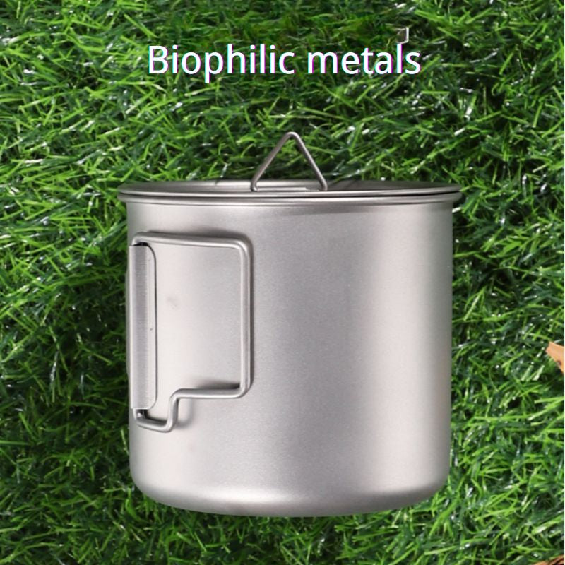Stainless steel camping pot on grass with 'Biophilic metals' text