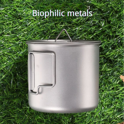 Stainless steel camping pot on grass with 'Biophilic metals' text