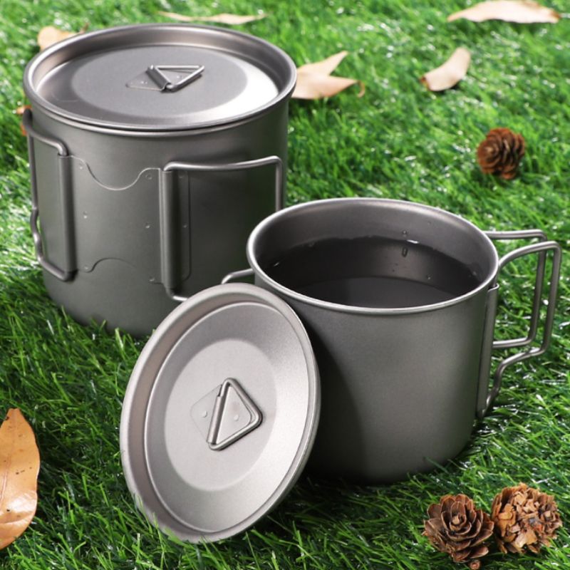 Two gray metal camping mugs on grass with pine cones.