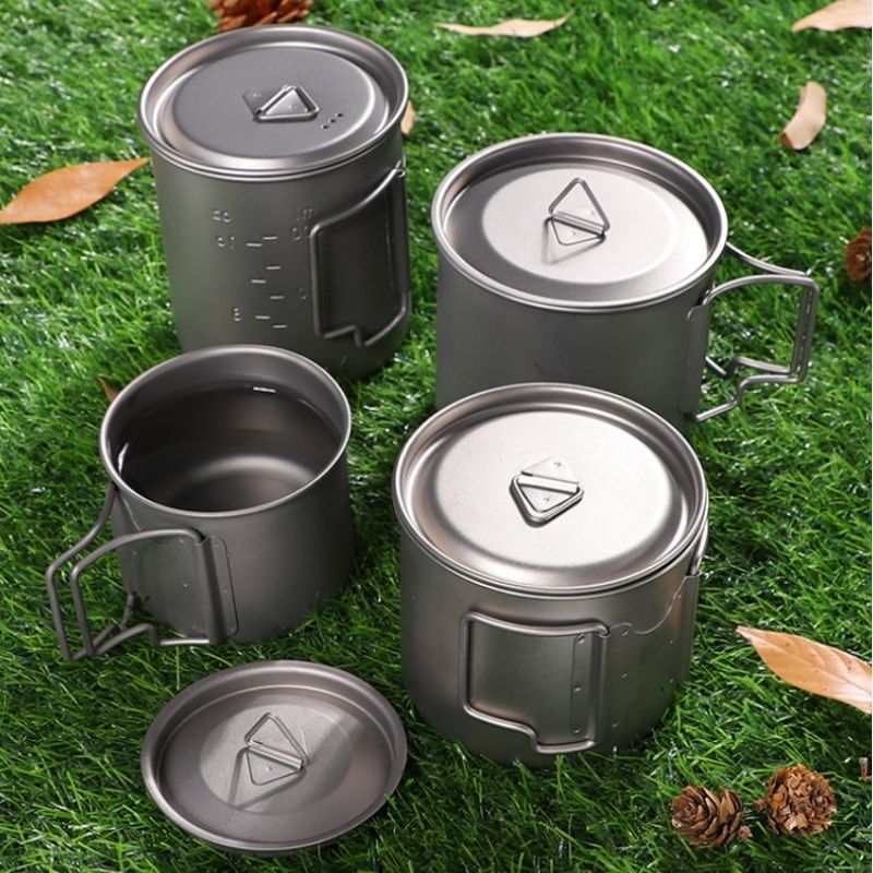 Set of four gray metal camping mugs on grass with pine cones.