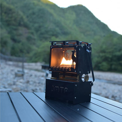 Portable camping stove with a lit flame on a wooden surface, mountainous background