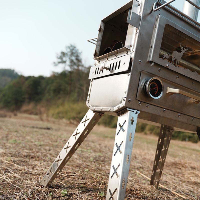 Metallic outdoor cooking stove on a stand in a field with trees in the background