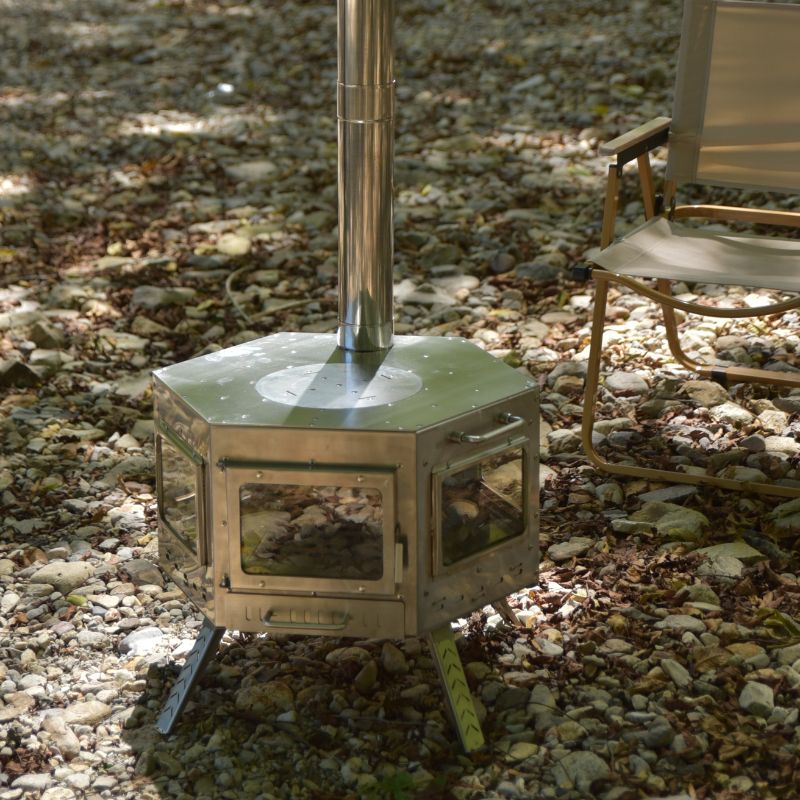 Hexagonal metal stove on a gravel surface with a chair in the background