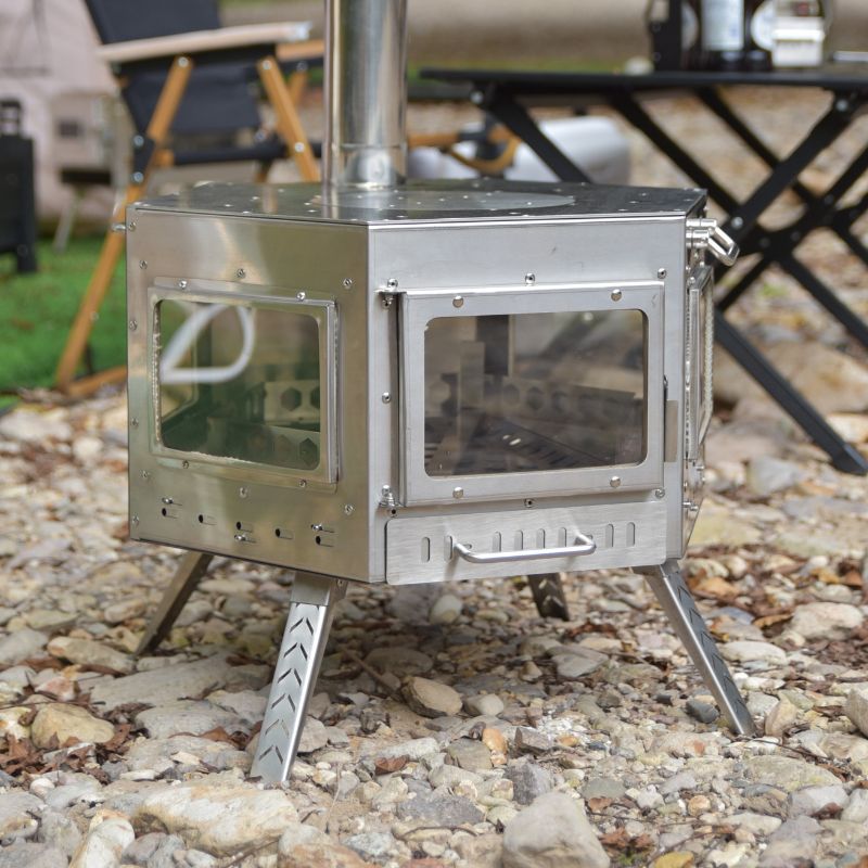 Metallic camping stove on a rocky ground with outdoor furniture in the background