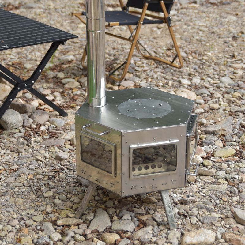 Portable metal stove on a rocky ground with chairs in the background