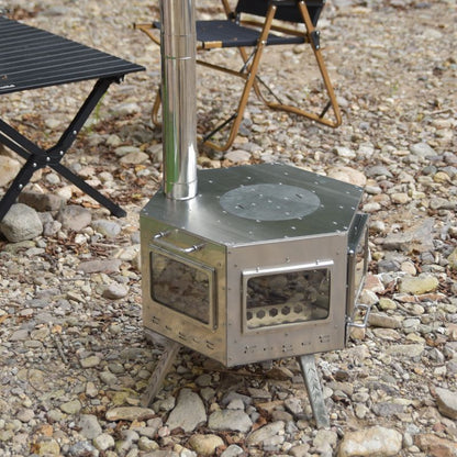 Portable metal stove on a rocky ground with chairs in the background