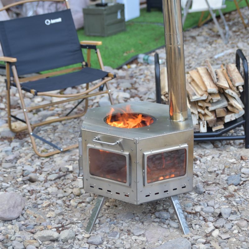 Portable wood stove with fire burning, surrounded by outdoor furniture and woodpile.