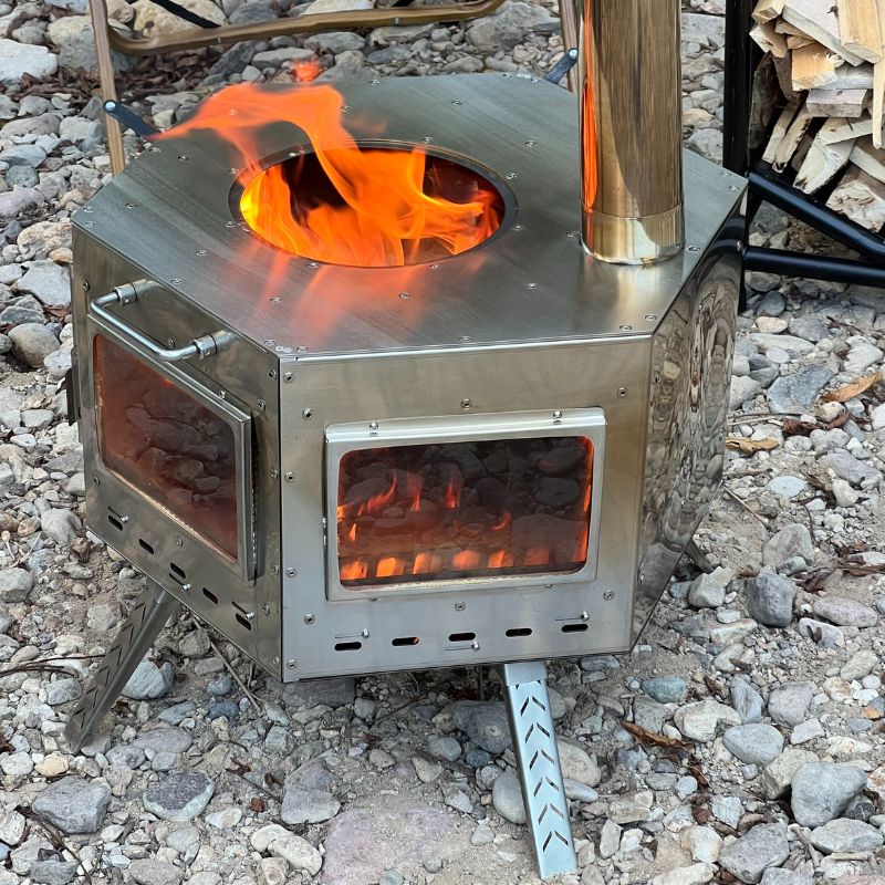 Metallic camping stove with flames on a rocky ground