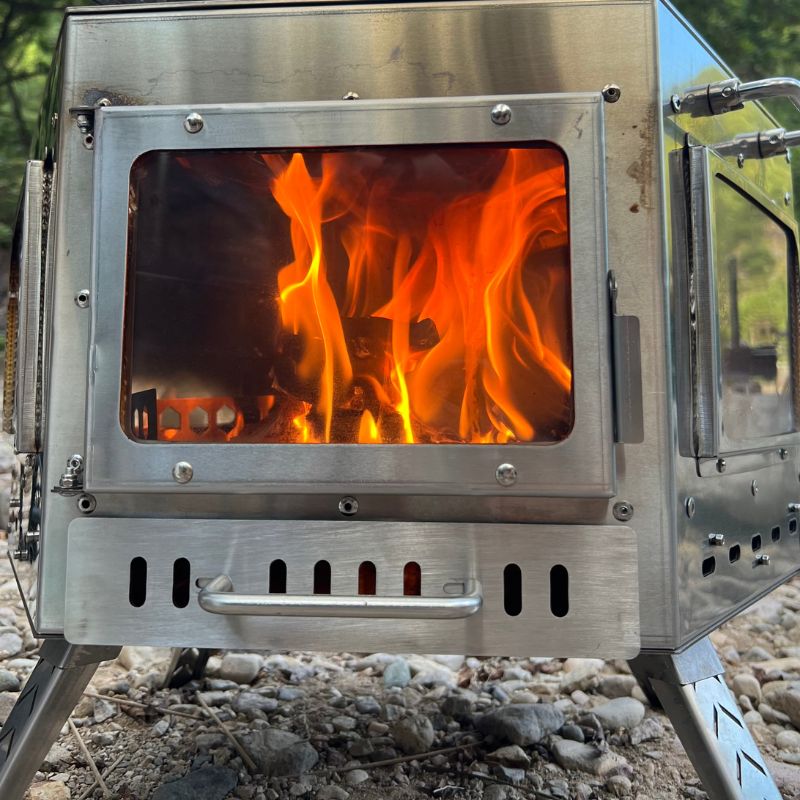 Metallic stove with flames inside, set against a natural outdoor background.