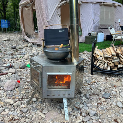 Camping stove with a pot over an open flame on a rocky ground with tents in the background.