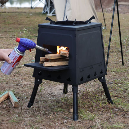 Person using a butane torch to light wood in a black outdoor stove in a natural setting.