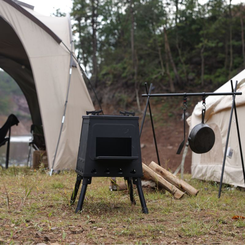 Camping stove with pots and pans in front of a tent in a forest setting