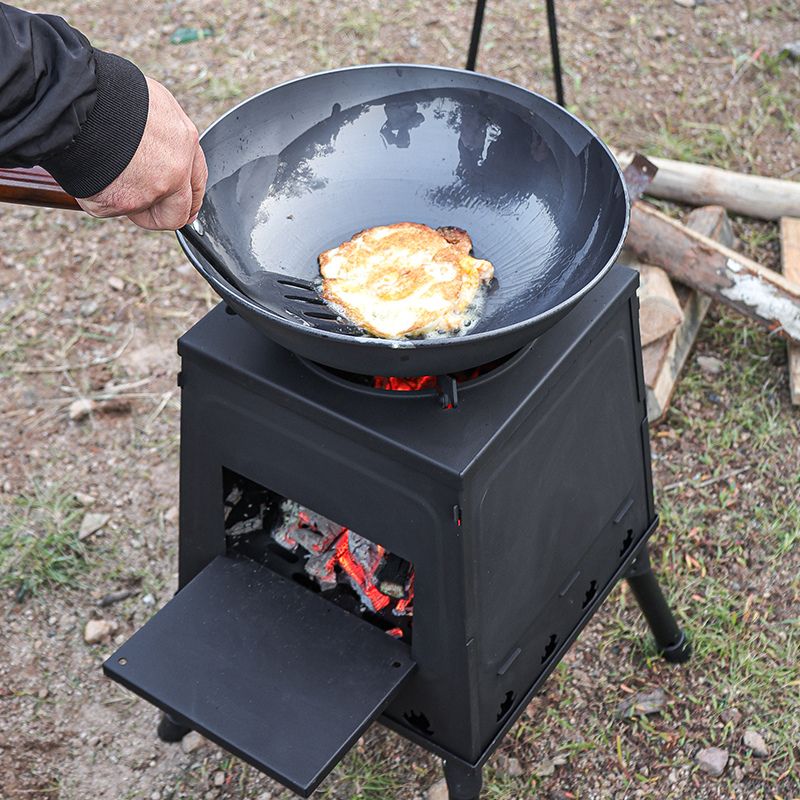 Person cooking on a portable stove with a frying pan over an open flame outdoors.