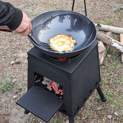 Person cooking on a portable stove with a frying pan over an open flame outdoors.