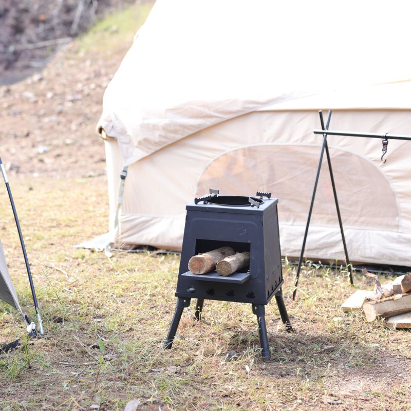 Black camping stove with logs in front of a tent in a natural setting