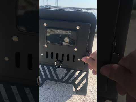 Hand holding black carbon steel portable camping wood stove with glass viewing window and folding legs outdoors