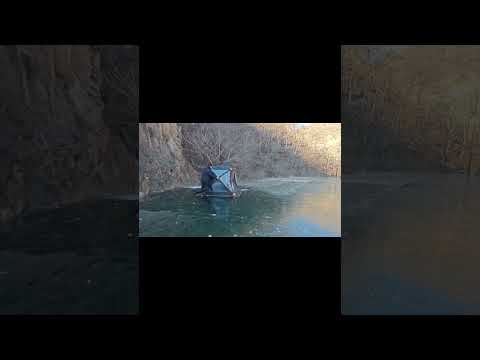 Person setting up a black insulated push-pull ice fishing tent on a frozen lake during winter