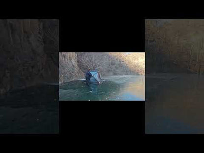 Person setting up a black insulated push-pull ice fishing tent on a frozen lake during winter