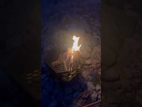 Burning fire in a black portable octagonal fire pit at night, creating a warm camping atmosphere outdoors