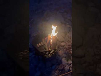 Burning fire in a black portable octagonal fire pit at night, creating a warm camping atmosphere outdoors