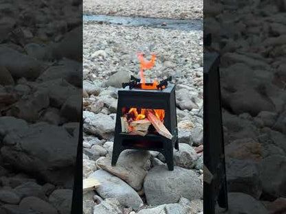 Black collapsible camping wood stove with glass viewing window and folding legs, setup outdoors.